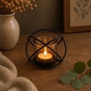 Centrepiece Iron Votive Candle Holder – 1 Cup Single Ball with a softly glowing tealight candle in an amber glass holder, set within a black metal sphere and displayed on a rustic wooden table in a warm, calming slow living interior.