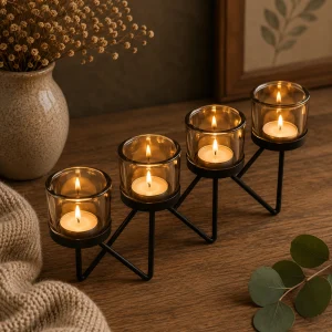 Centrepiece Iron Votive Candle Holder – 4 Cup Zig Zag with four softly glowing tealight candles in amber glass holders on a black metal stand, displayed on a rustic wooden table in a warm, calming slow living interior.
