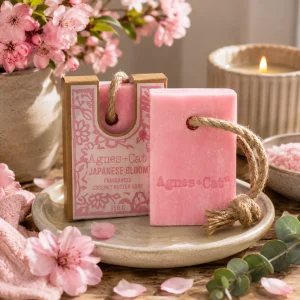 Agnes + Cat Soap on a Rope – Japanese Bloom displayed on a ceramic soap dish with delicate cherry blossom flowers, soft linen and eucalyptus, creating a peaceful spa-inspired bathroom scene in warm natural light with a calming slow living atmosphere.
