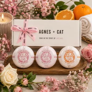 Agnes + Cat Floral & Citrus Bath Fizzer Gift Set displayed in a luxury presentation box with Cherry Blossom, Wild Rose and Clementine bath fizzers, surrounded by fresh flowers, citrus fruit, soft towels and a glowing candle in an elegant spa-inspired slow living setting.