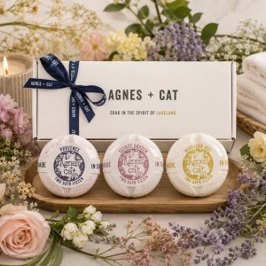 Agnes + Cat Secret Garden Bath Fizzer Gift Set displayed in a luxury presentation box with Provence, Secret Garden and Northern Rose bath fizzers, surrounded by fresh flowers, lavender, soft towels and a glowing candle in an elegant spa-inspired slow living setting.