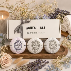 Agnes + Cat Signature Fragrance Bath Fizzer Gift Set displayed in a luxury presentation box with Provence, Sea Salt & Moss and Windermere bath fizzers, surrounded by dried flowers, lavender, soft towels and a glowing candle in an elegant spa-inspired slow living setting.