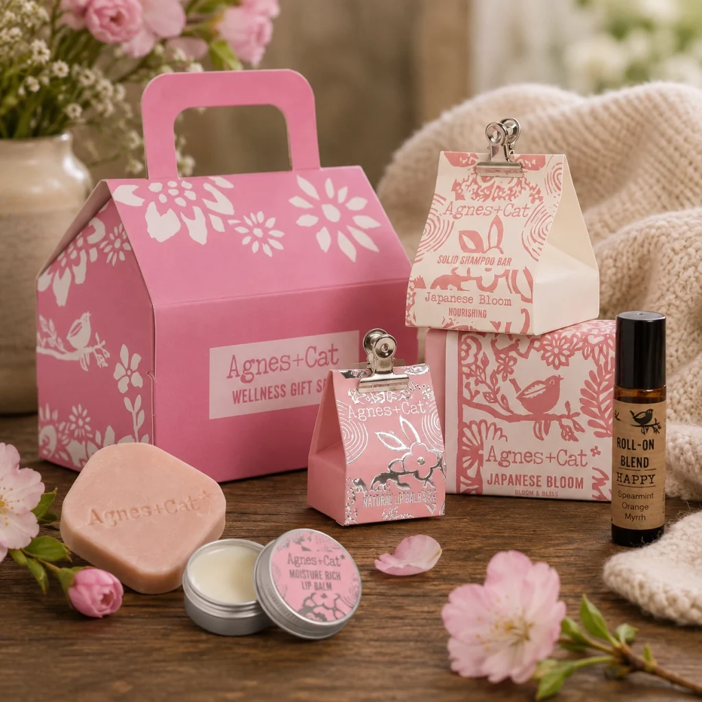 Bloom & Bliss Wellness Gift Set displayed on a rustic wooden table with natural soap, nourishing lip balm, aromatherapy roll-on, Japanese Bloom shampoo bar, soft flowers and cosy linen in a calming slow living setting.