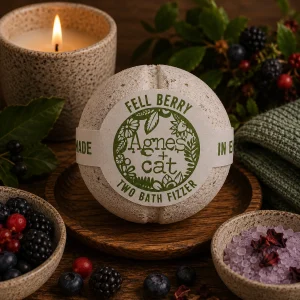 Fell Berry luxury bath fizzer by Agnes + Cat displayed on a rustic wooden tray with fresh blackberries, blueberries and red berries, botanical bath salts, soft linen and a glowing candle in a calming spa-inspired slow living setting.