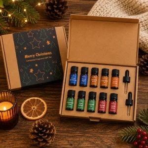 Festive Delights Luxury Christmas Fragrance Oil Gift Set displayed on a rustic wooden table with an open presentation box containing ten festive fragrance oils and two glass droppers, surrounded by pine branches, pine cones, dried orange, warm candlelight and soft knitted textures in a cosy Christmas slow living setting.