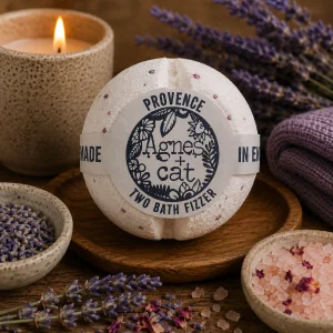 Provence luxury bath fizzer by Agnes + Cat displayed on a rustic wooden tray with dried lavender, lavender buds, pink bath salts, soft linen and a glowing candle in a calming spa-inspired slow living setting.