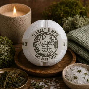 Sea Salt & Moss luxury bath fizzer by Agnes + Cat displayed on a rustic wooden tray with natural sea salt crystals, preserved moss, dried seaweed, soft linen and a glowing candle in a calming coastal-inspired spa setting.