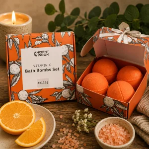Vitamin C Bath Bomb Gift Set with four citrus essential oil bath bombs displayed in an orange presentation box on a rustic wooden table with fresh orange slices, bath salts, soft linen, wildflowers and a glowing candle in a calming spa-inspired slow living setting.