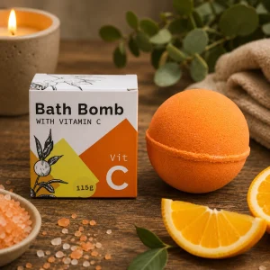 Vitamin C Bath Bomb with Orange, Lemon & Essential Oils displayed beside its presentation box on a rustic wooden table with fresh citrus slices, bath salts, soft linen and a glowing candle in a calming spa-inspired slow living setting.