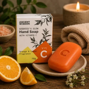 Vitamin C Hand Soap with Orange & Lemon Essential Oils displayed beside its presentation box on a ceramic soap dish with fresh orange slices, botanical greenery, soft linen and a glowing candle in a calming spa-inspired slow living setting.