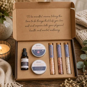 Serenity Essential Self-Care Kit displayed open on a rustic wooden table, containing strawberry body scrub, rejuvenating body cream, Vitamin C facial serum and three bath salt vials labelled Energise, Sensual and Clarity.